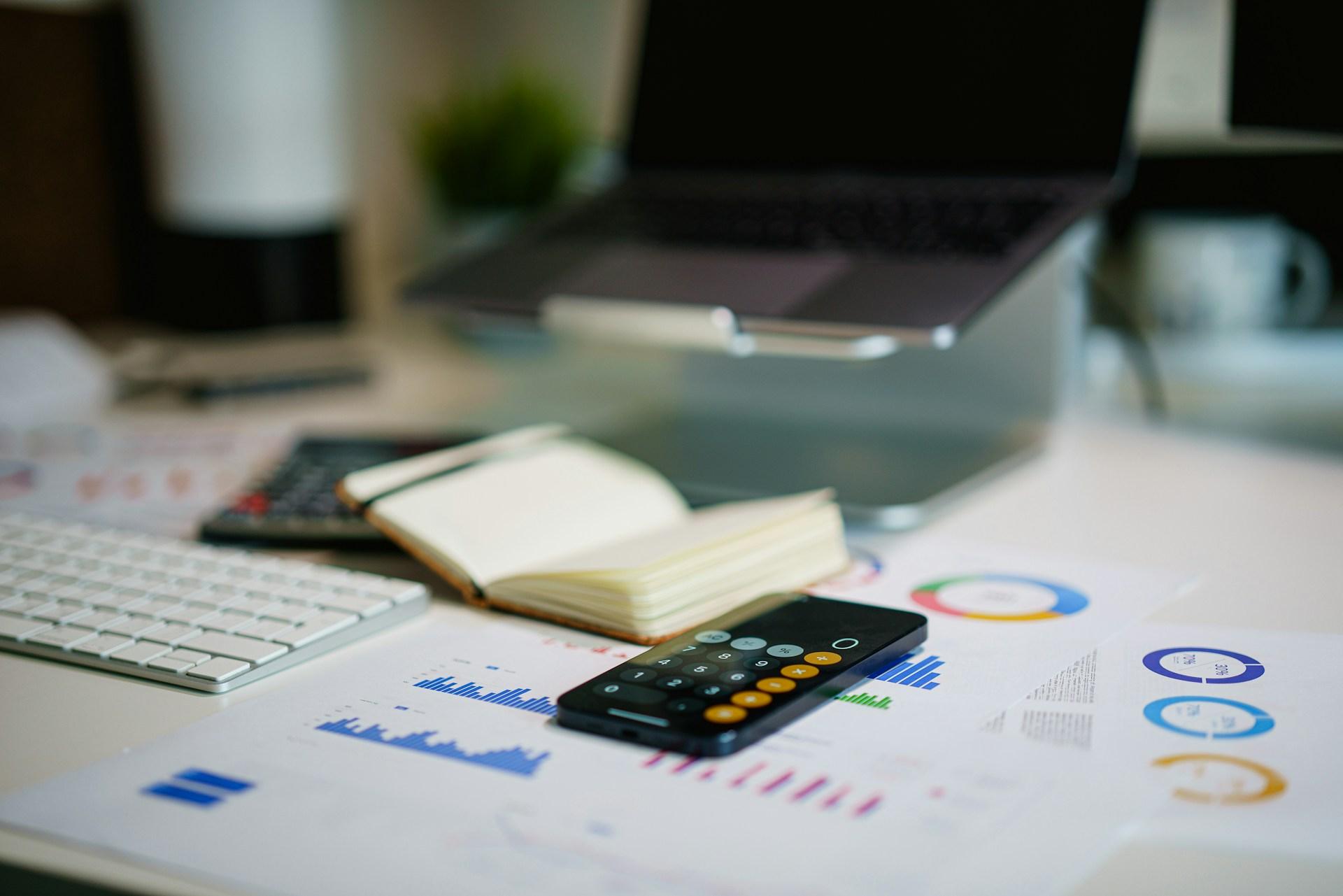Financial charts, a smartphone calculator and a notebook on an office desk