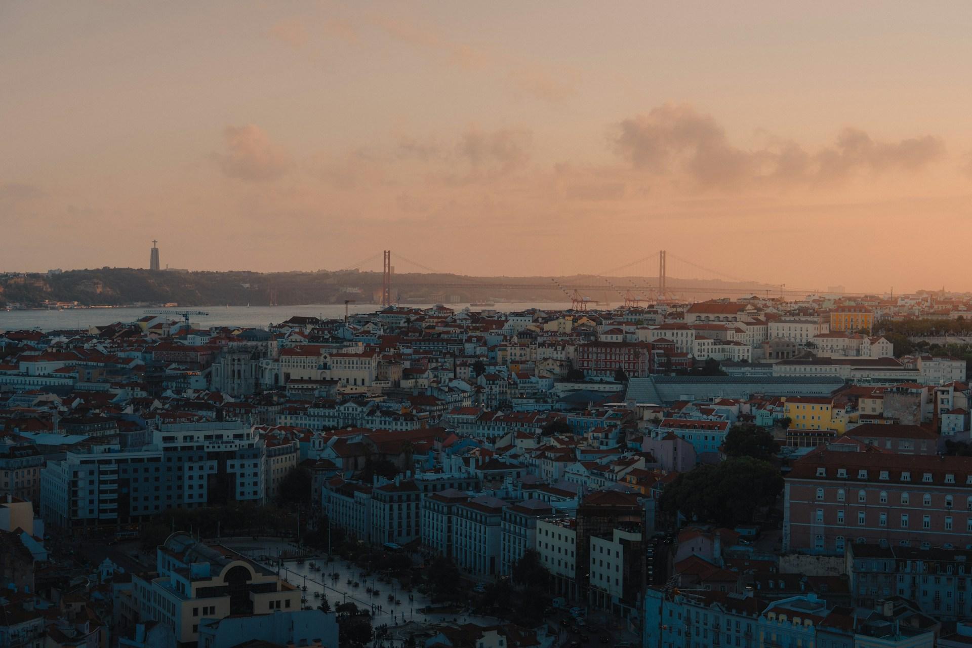 Lisbon rooftops overlooking the Tagus River and the 25 de Abril Bridge at sunset