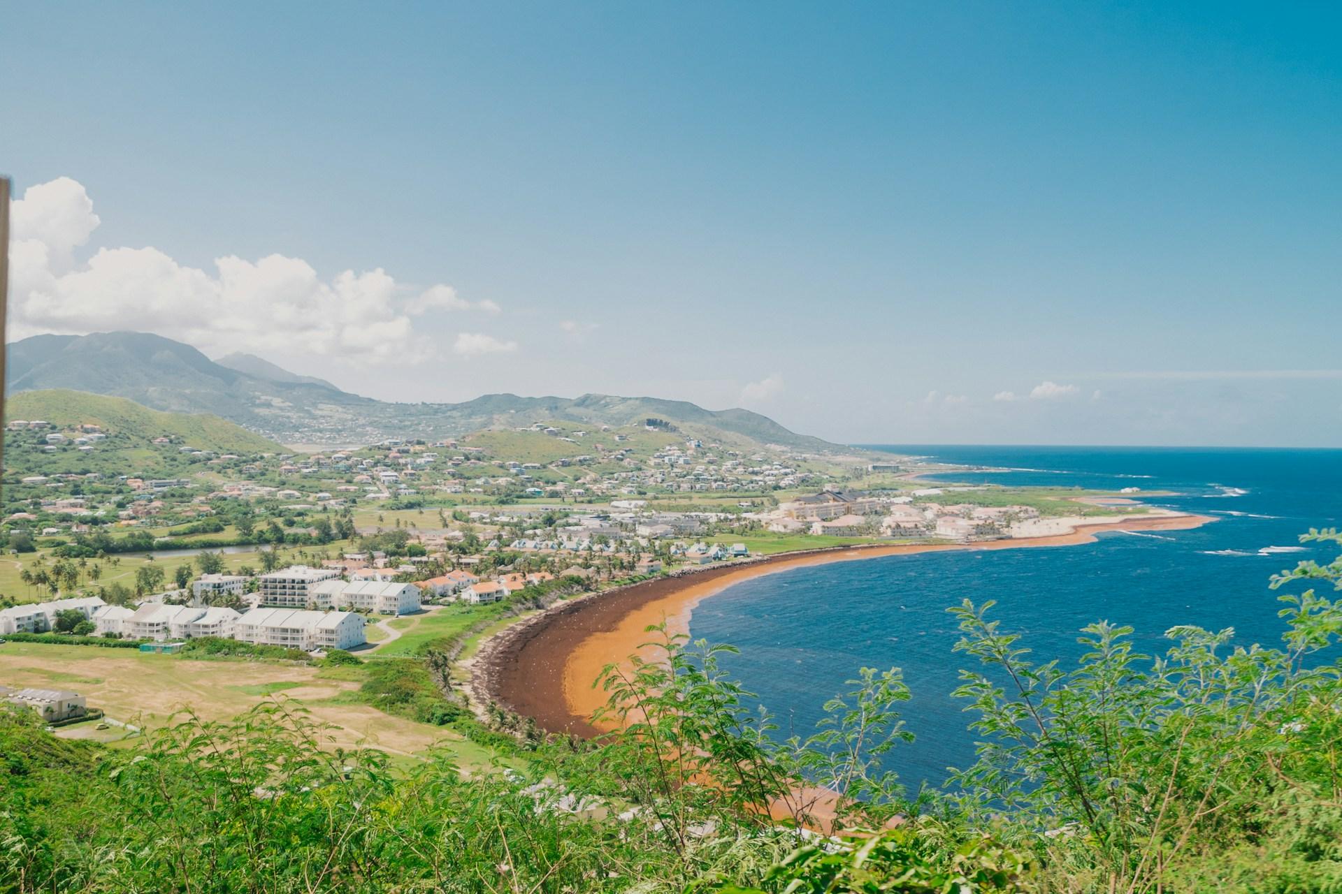 Curving beach, coastal neighbourhoods and green hills beside the blue sea in St Kitts and Nevis