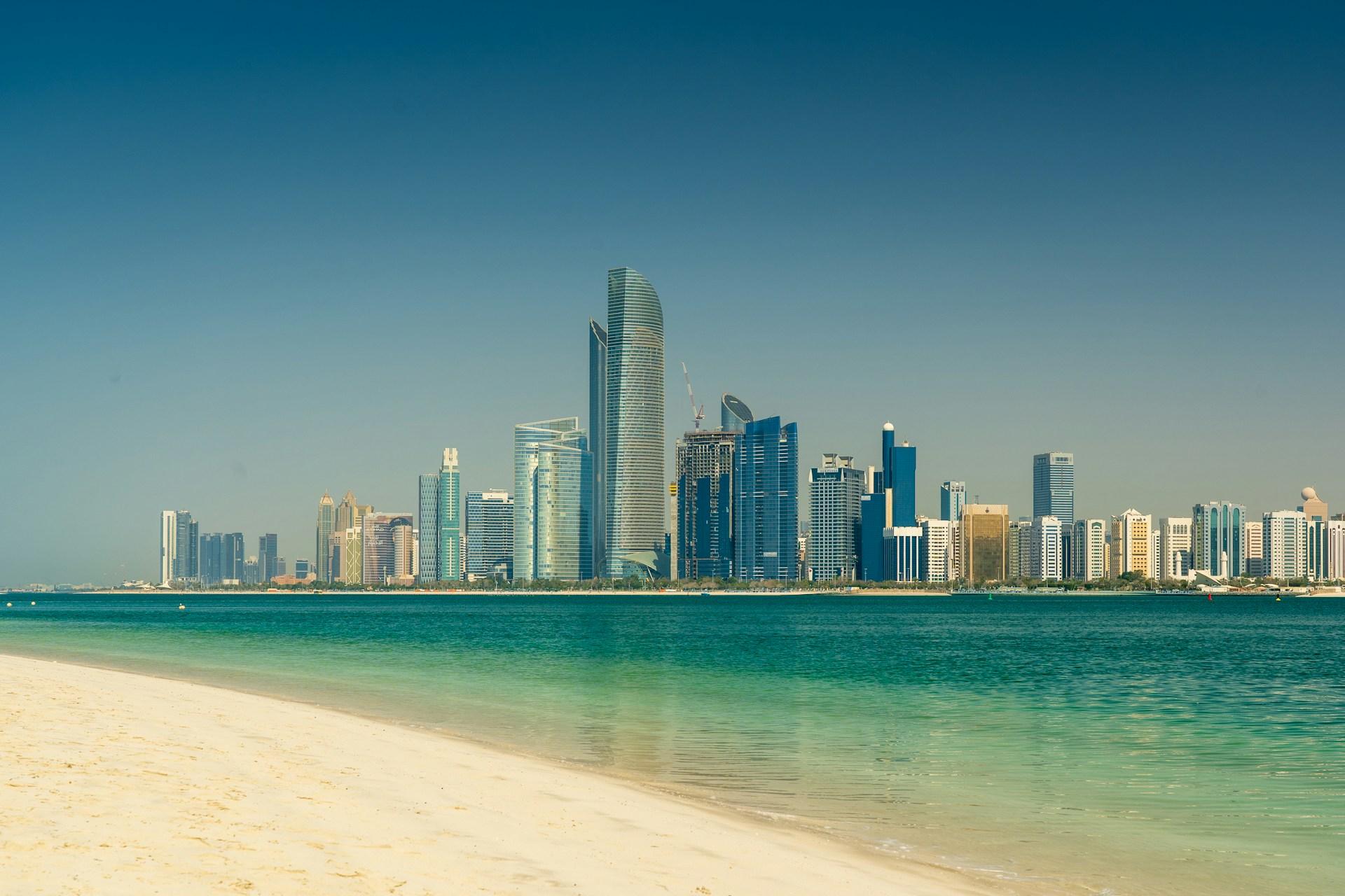 Abu Dhabi skyline across turquoise water and a sandy beach in the United Arab Emirates