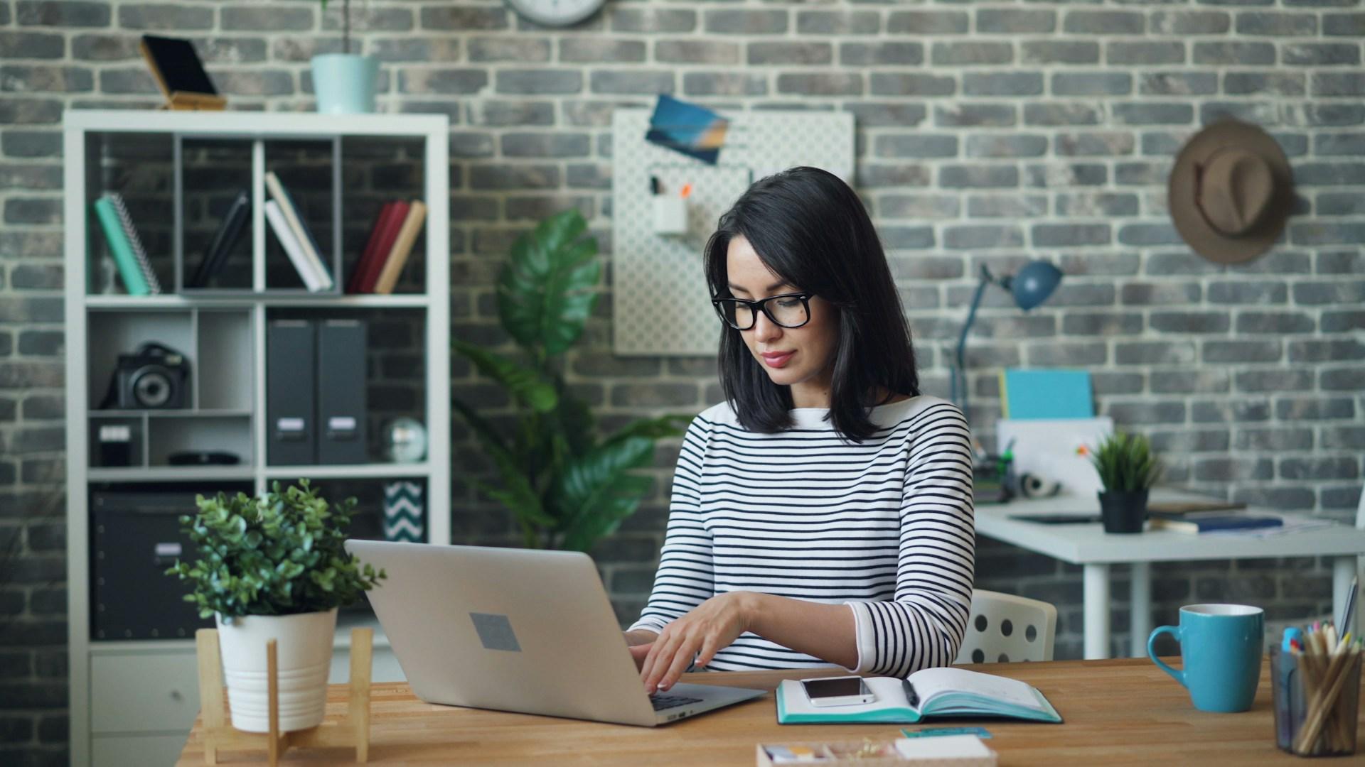 A woman working at a laptop beside a notebook in an office